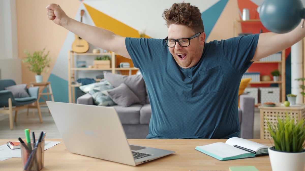 joyful young businessman celebrating success at work using laptop at home having fun spinning on chair. Happiness and business concept.
